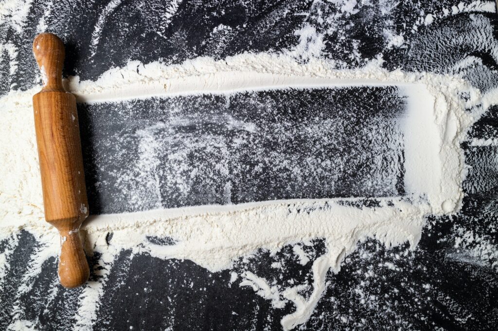 Rolling pin and white flour on dark table. Baking background